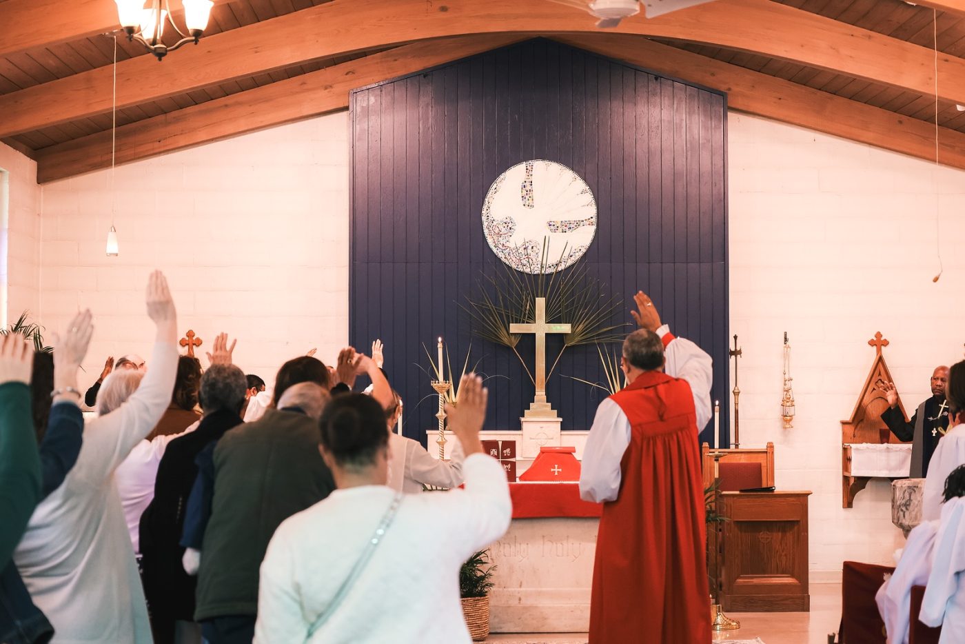 Congregants raise their hands during the Palm Sunday blessing of the dove mosaic at Holy Comforter.